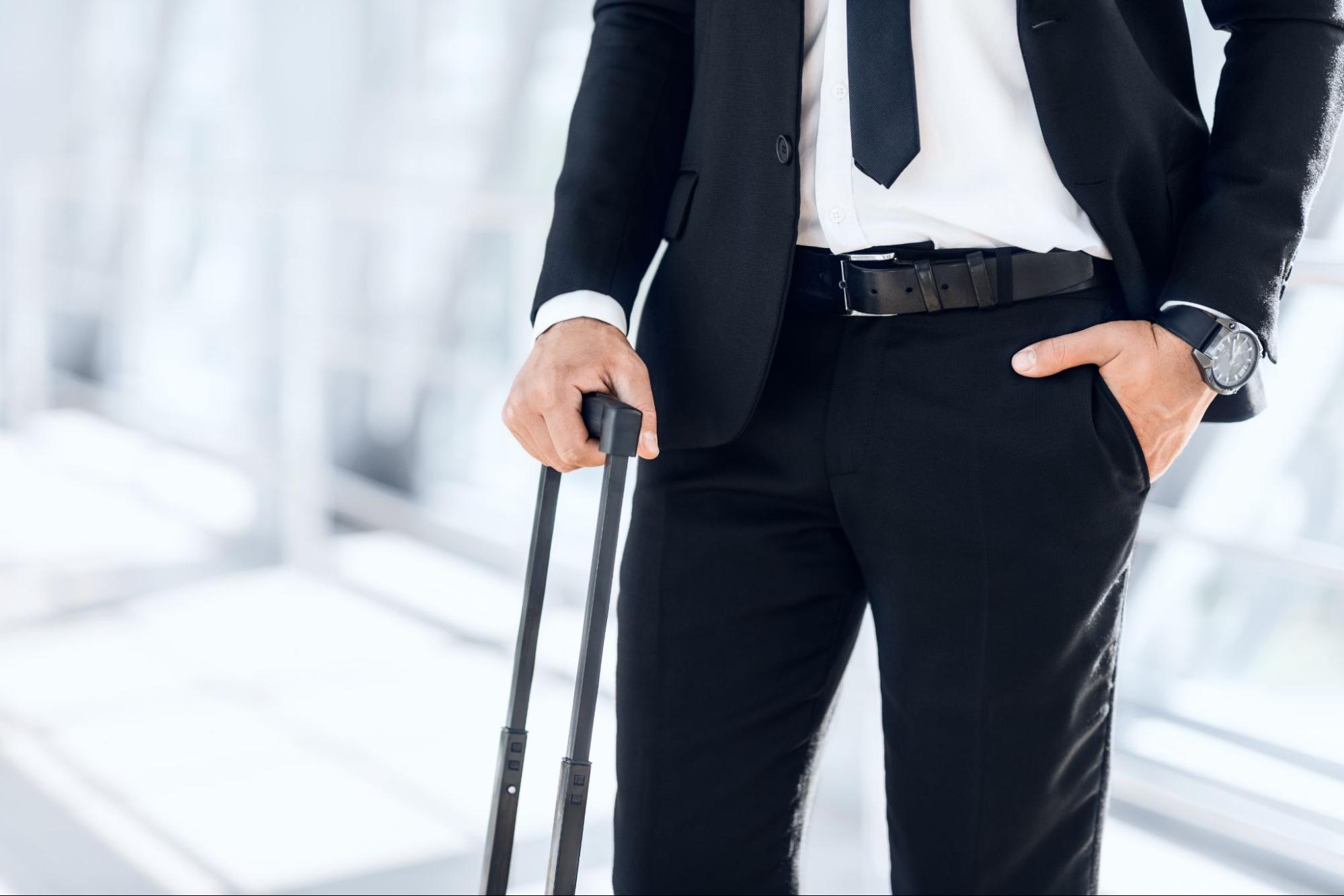 A man wearing a suit with his suitcase standing at an airport