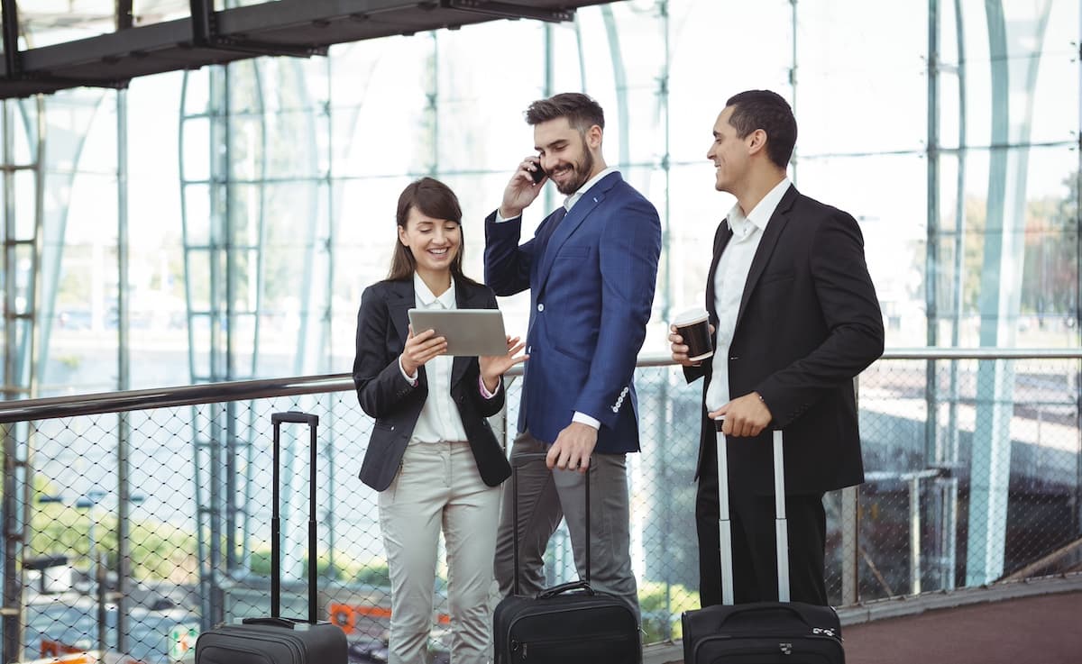Three business travellers using an online booking platform on a tablet at the airport