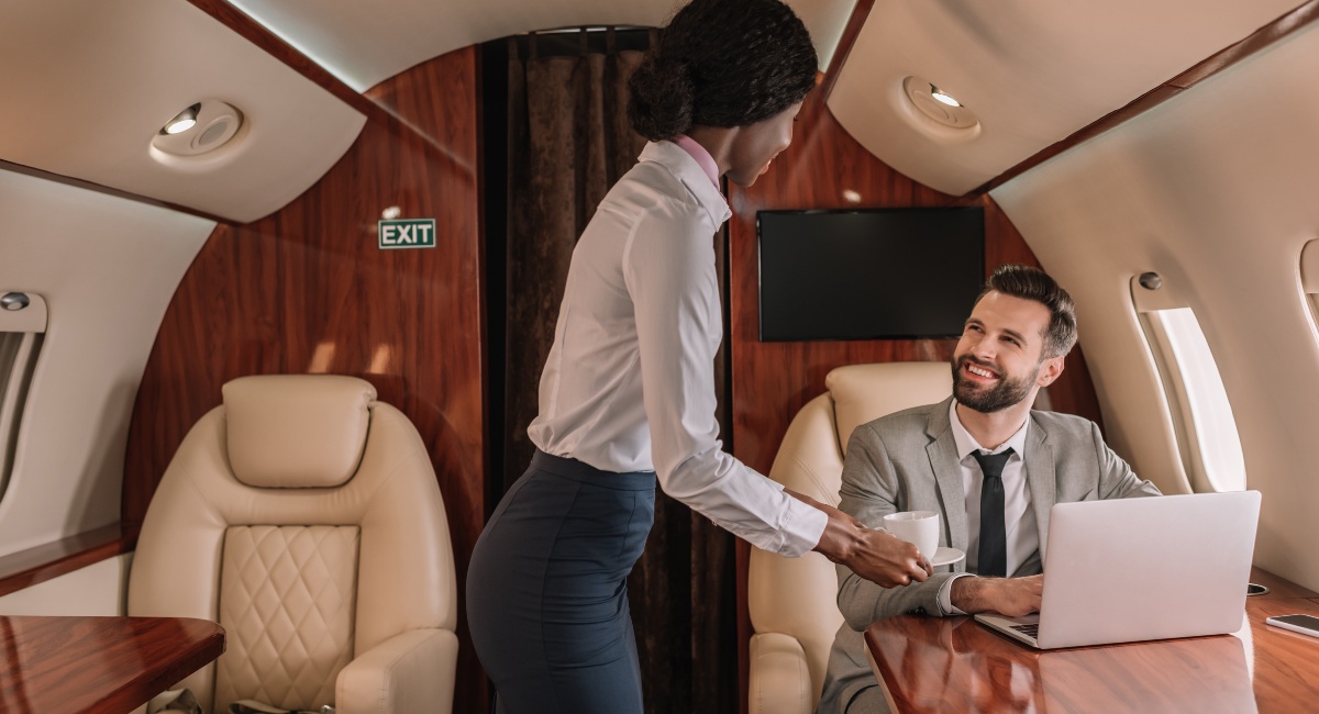 Flight attendant serving coffee to a businessman on a luxurious private jet with plush seating and sophisticated interior, emphasizing top-tier service in private jet rentals.
