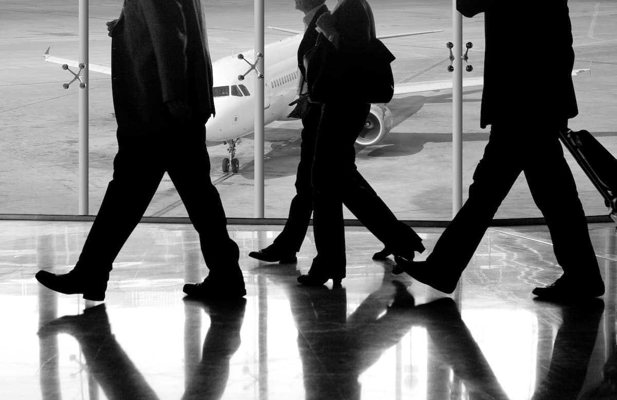 People walking in suits through airport with plane in background
