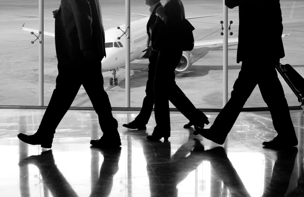 People in suits walking through an airport with a plane in the background