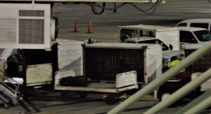 An airport scene at night shows workers in blurry motion loading luggage onto carts